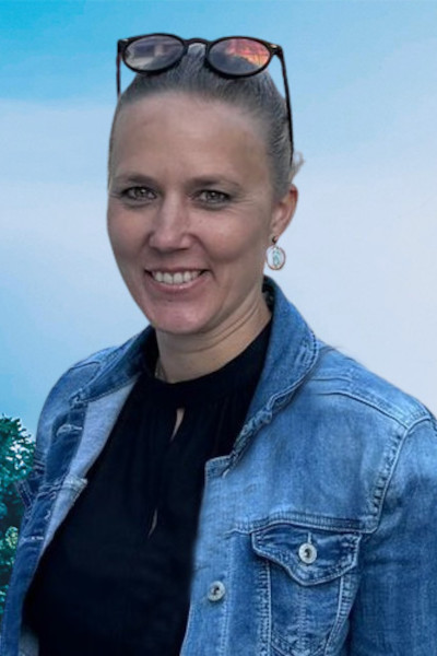 Lächelnde Frau mit Brille und blauer Jeansjacke vor blauem Hintergrund
